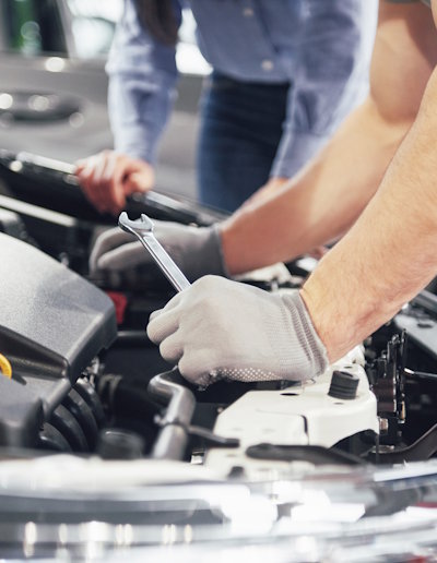 A man mechanic and woman customer look at the car hood and discuss repairs.